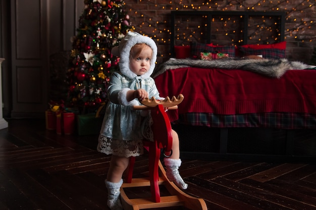 Gelukkig schattig mooi klein meisje zit op een vintage houten chairdeer met kerstversiering