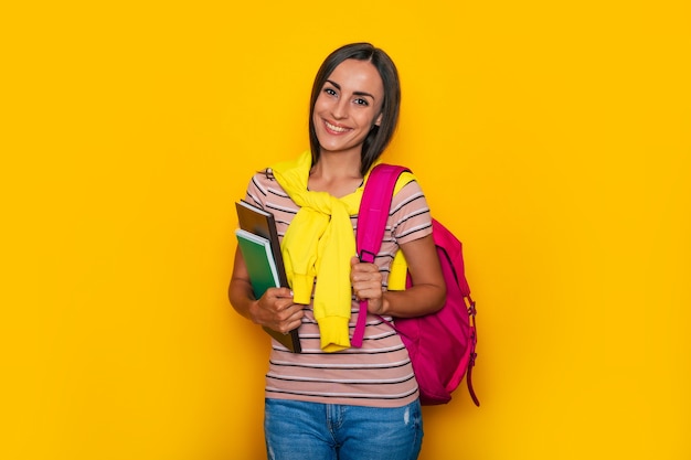 Gelukkig schattig studentenmeisje in moderne vrijetijdskleding met roze rugzak poseert in studio