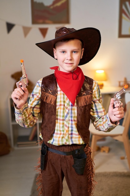Gelukkig schattige kleine jongen in kostuum van cowboy poseren met twee revolvers