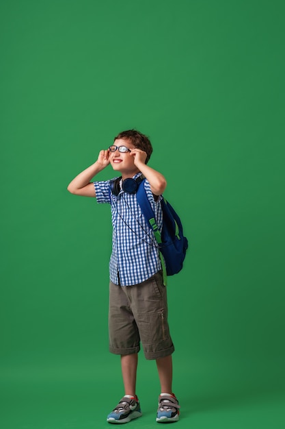 Gelukkig schattige slimme jongen in glazen met schooltas en hoofdtelefoon