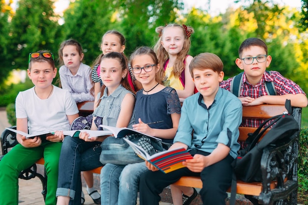 Gelukkig schoolgenoten portret. Schoolgenoten zitten met boeken in een houten bankje in een stadspark en studeren op zonnige dag.