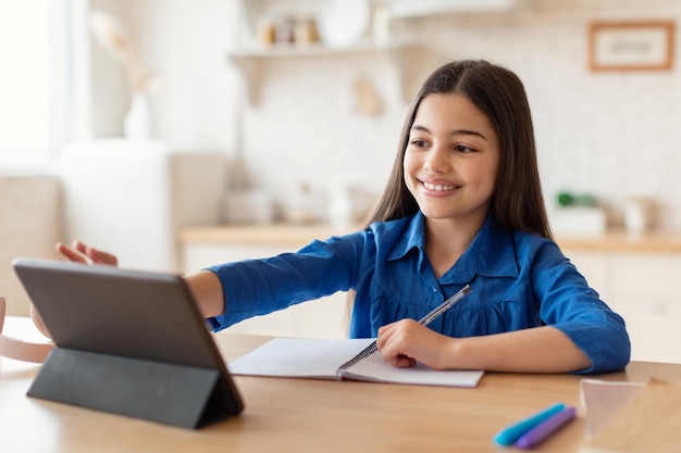 Gelukkig schoolmeisje dat digitale tablet gebruikt die huiswerk online thuis doet