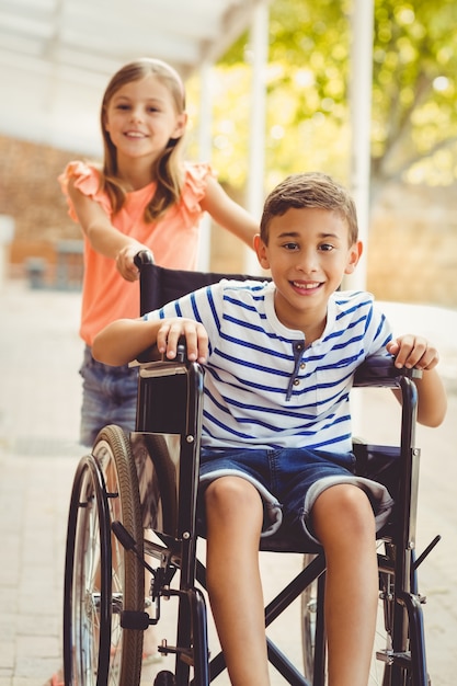 Gelukkig schoolmeisje dat een jongen op rolstoel duwt