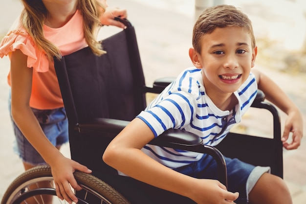 Gelukkig schoolmeisje dat een jongen op rolstoel duwt