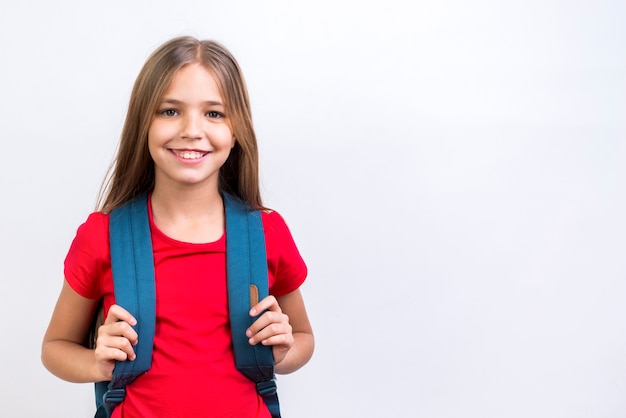 Gelukkig schoolmeisje die met rugzak bij camera glimlachen