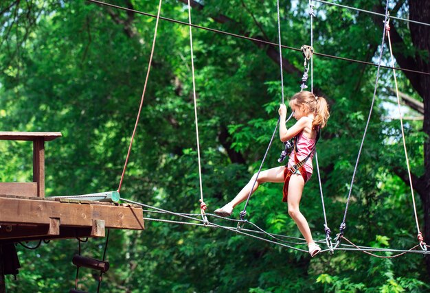 Gelukkig schoolmeisje die van activiteit in een klimavonturenpark genieten op een de zomerdag,