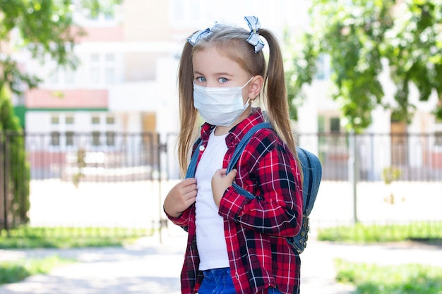 Gelukkig schoolmeisje in een beschermend masker met een rugzak. in een wit T-shirt en een geruit overhemd