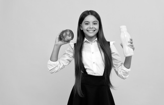 Gelukkig schooltienermeisje in uniform houdt appel en waterfles gezond vast