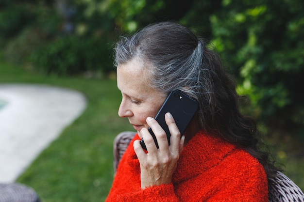 Foto gelukkig senior blanke vrouw praten over smartphone in de tuin