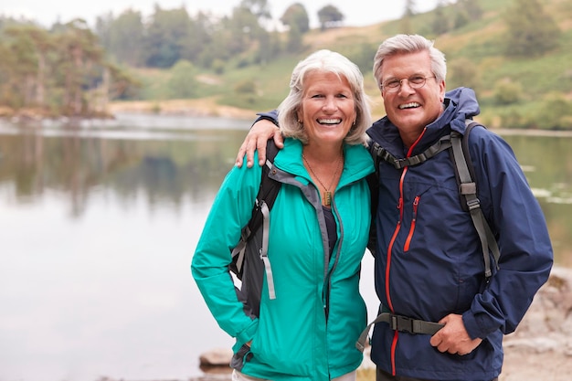 Gelukkig senior koppel dat aan de oever van een meer staat en lacht naar de camera Lake District UK