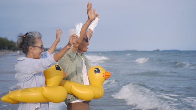 Gelukkig senior koppel draagt een rubberen ring, zet een medisch gezichtsmasker af en rent naar het strand