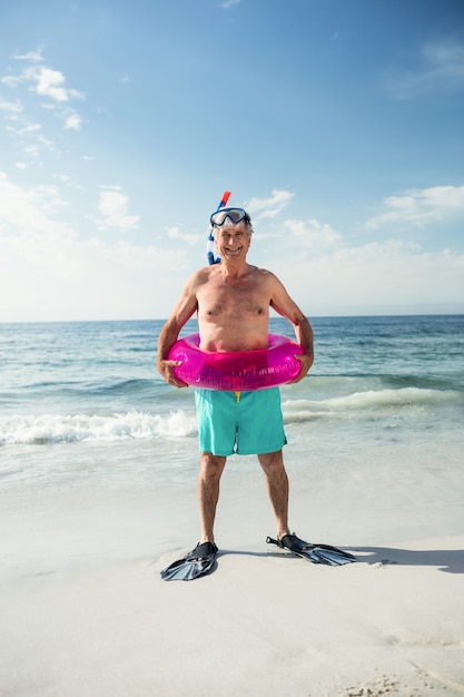 Gelukkig senior man in opblaasbare ring en flippers permanent op strand
