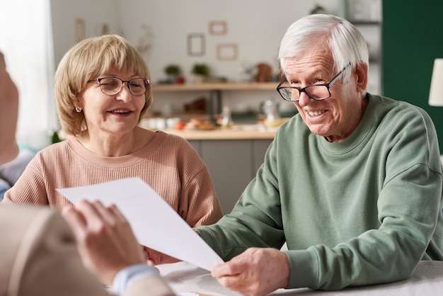 Foto gelukkig senior paar dat een contract ondertekent en met consultant praat tijdens een ontmoeting thuis