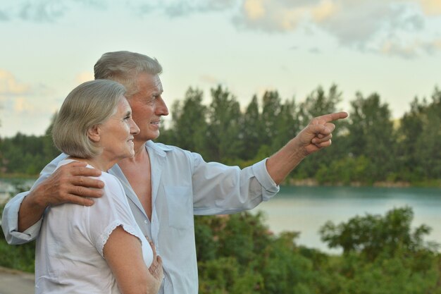 Gelukkig senior paar in de buurt van rivier in de zomer, man wijzend met zijn hand