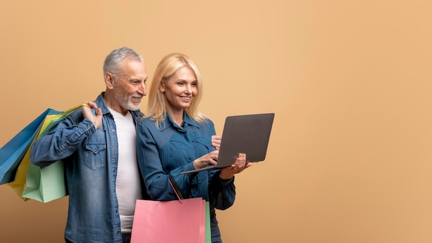 Gelukkig senior paar met boodschappentassen en laptop op beige