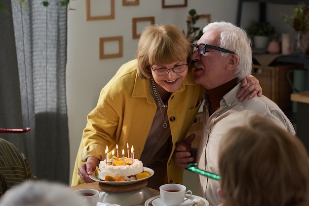 Gelukkig senior paar omarmen aan tafel terwijl ze hun verjaardag vieren met taart thuis