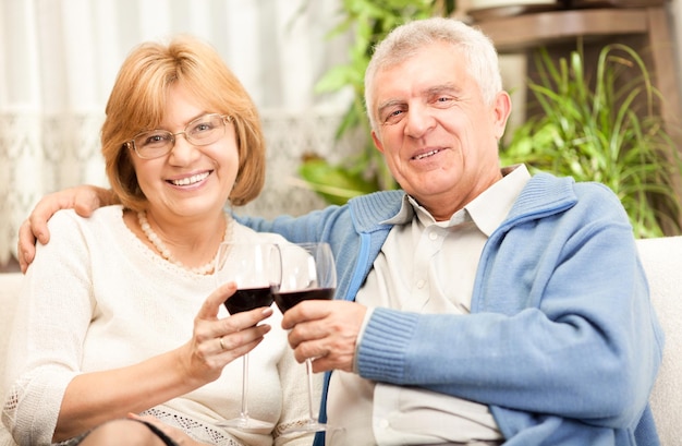 Gelukkig senior paar roosteren hun verjaardag met rode wijn thuis ambient