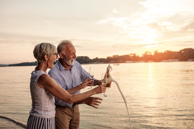 Gelukkig senior paar vieren met champagne aan de rivieroever