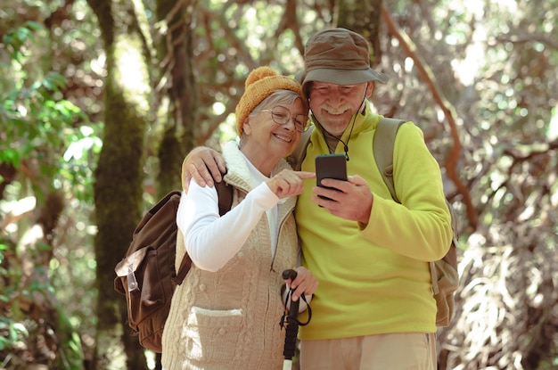 Gelukkig senior paar wandelen in het bos met rugzakken met behulp van mobiele telefoon knappe gepensioneerden genieten van vrijheid en natuur