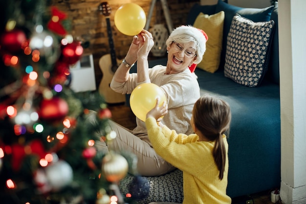 Gelukkig senior vrouw en haar kleindochter spelen met ballonnen tijdens eerste kerstdag