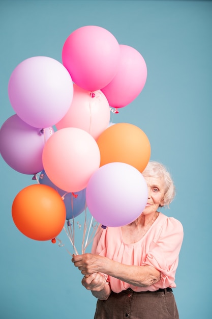 Gelukkig senior vrouw gluren uit bos van kleurrijke ballonnen geïsoleerd