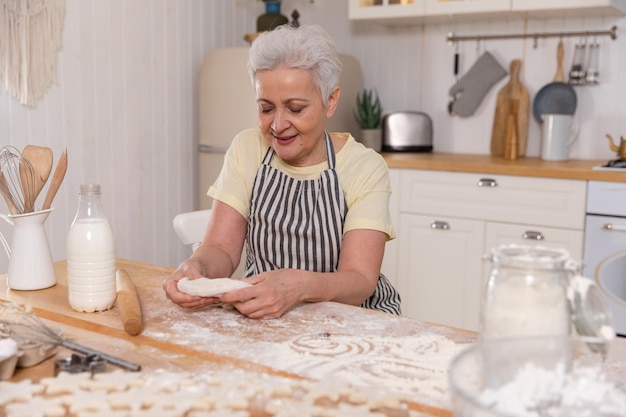 Gelukkig senior vrouw koken in de keuken stijlvolle oudere volwassen grijsharige dame grootmoeder deeg kneden