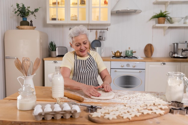 Gelukkig senior vrouw koken in de keuken stijlvolle oudere volwassen grijsharige dame grootmoeder deeg kneden