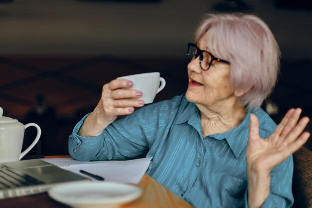 Gelukkig senior vrouw met bril zit aan een tafel voor een laptop Gepensioneerde vrouw ongewijzigd chatten