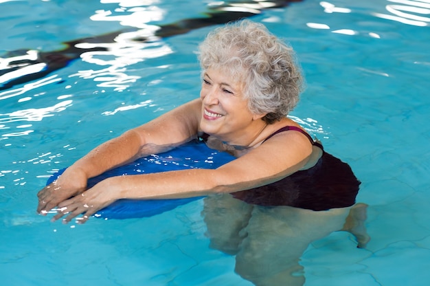 Gelukkig senior vrouw met kickboard in een zwembad