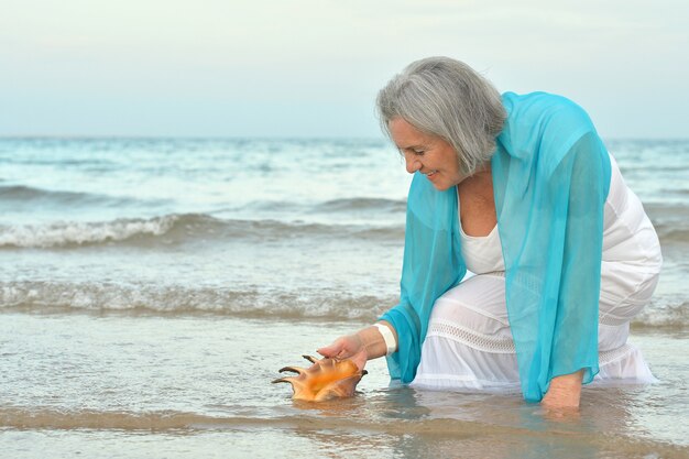 Gelukkig senior vrouw met shell op strand