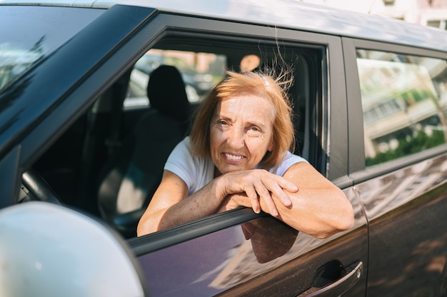 Gelukkig senior vrouw rijden zittend in nieuwe bruine auto glimlachend kijken naar camera genieten van