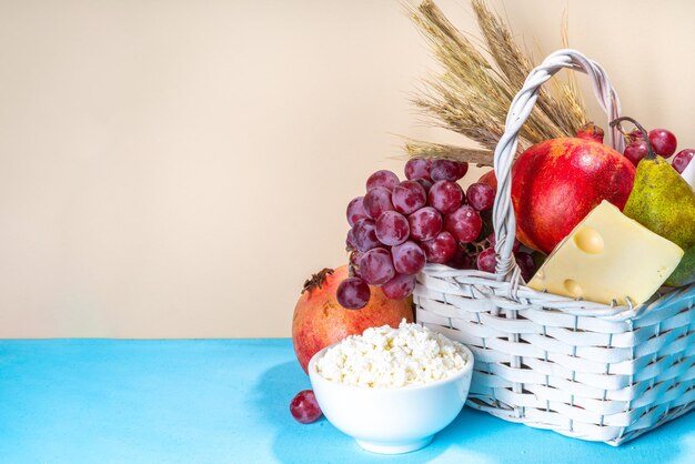 Gelukkig Sjavoeot wenskaart achtergrond met voedsel symbolen van Joodse Sjavoeot vakantie granaatappel druiven appel zoete challah brood tarwe spikelets melk kaas kwark op lichtblauwe achtergrond