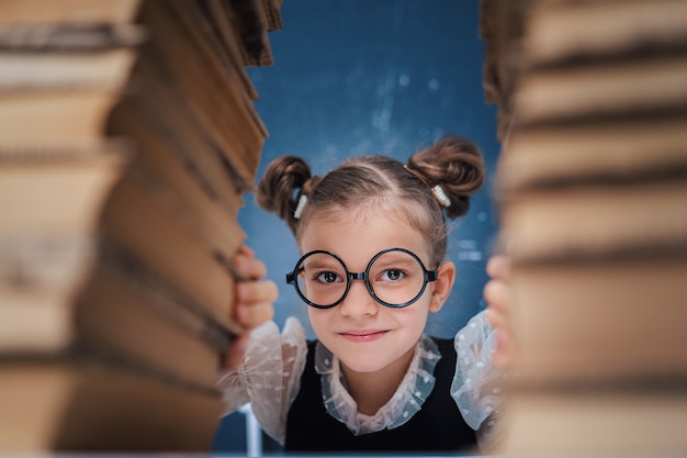 Foto gelukkig slim meisje dat in ronde glazen tussen twee stapels boeken zit