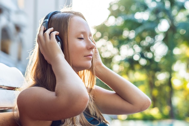 Gelukkig smartphone vrouw ontspannen in de buurt van zwembad luisteren met oordopjes naar streaming muziek. mooi meisje dat haar mobiele telefoon-app 4g-gegevens gebruikt om liedjes te spelen terwijl ze ontspant op luxe zomervakanties.