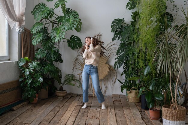 Foto gelukkig spaanse vrouw draagt draadloze hoofdtelefoons ontspannen dansen in huis tuin met tropische planten