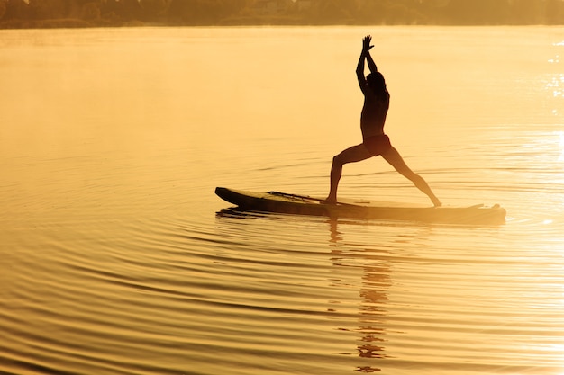 Gelukkig sportman doet yoga oefeningen op sup board buitenshuis.