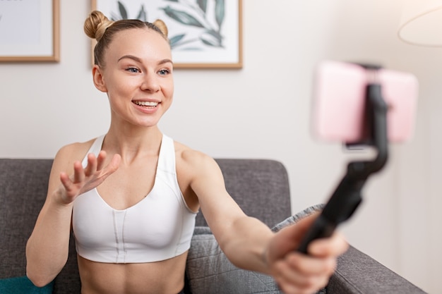 Gelukkig sportvrouw glimlachend en gebarend tijdens het opnemen van video voor fitness vlog thuis