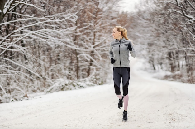 Gelukkig sportvrouw loopt in de natuur op besneeuwde winterdag. winterfitness, outdoor fitness, koud weer