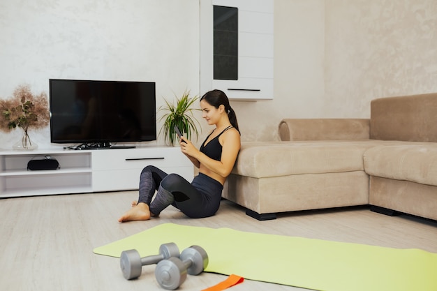 Gelukkig Sportvrouw met behulp van slimme telefoon na een training thuis.