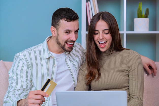 Gelukkig stel dat online winkelt met een creditcard, opgewonden terwijl ze naar een laptop kijken.