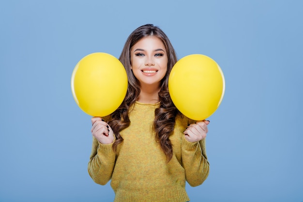 Gelukkig stijlvolle tiener die gele ballonnen toont en lacht voor de camera terwijl hij plezier heeft tegen blauwe ...