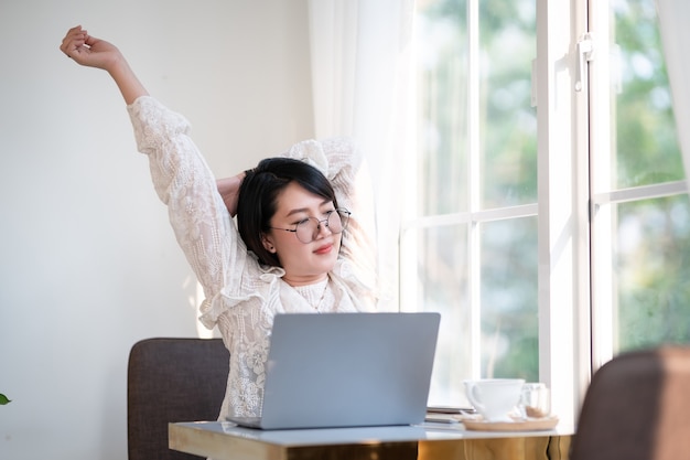 Gelukkig Stretching Ontspanning Rusten van Aziatische freelance mensen zakelijke vrouwelijke casual werken met laptopcomputer met koffiekopje en smartphone in coffeeshop de achtergrond, communicatieconcept