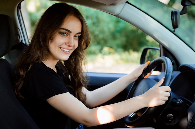 Gelukkig student in de bestuurdersstoel van een moderne auto glimlacht naar de camera