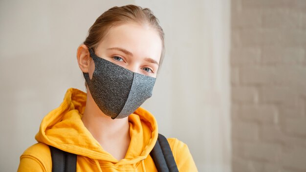 Gelukkig student op bakstenen muur jonge mooie vrouw glimlacht oprecht beschermend masker portret met rugzak tiener meisje blonde kaukasische tiener reiziger in masker lange webbanner kopie ruimte