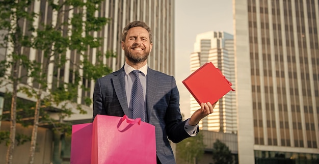 Foto gelukkig succesvolle man in formalwear zet huidige doos in boodschappentas buiten het kantoor winkelen