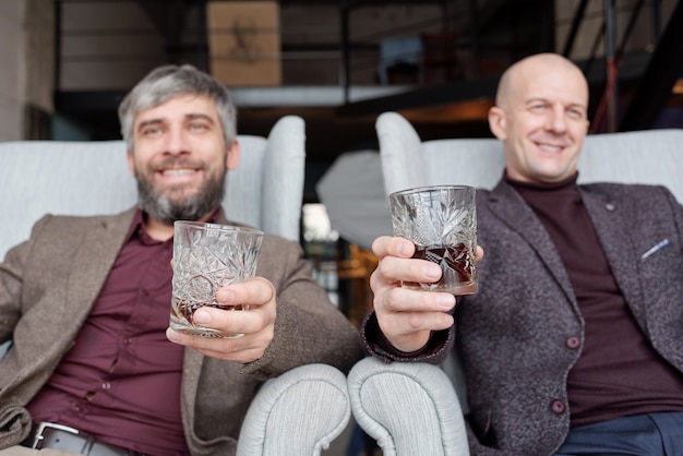 Gelukkig succesvolle mannen in modieuze outfits zitten in fauteuils en samen alcohol drinken