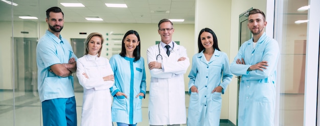 Gelukkig team van succesvolle en zelfverzekerde moderne artsen poseren en kijken op de camera naar de ziekenhuisgang