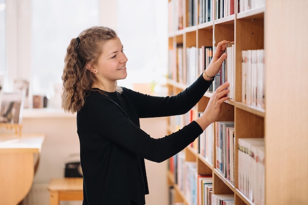 Gelukkig tenagemeisje of student die boek van plank in bibliotheek nemen - Mensen, kennis, onderwijs en schoolconcept