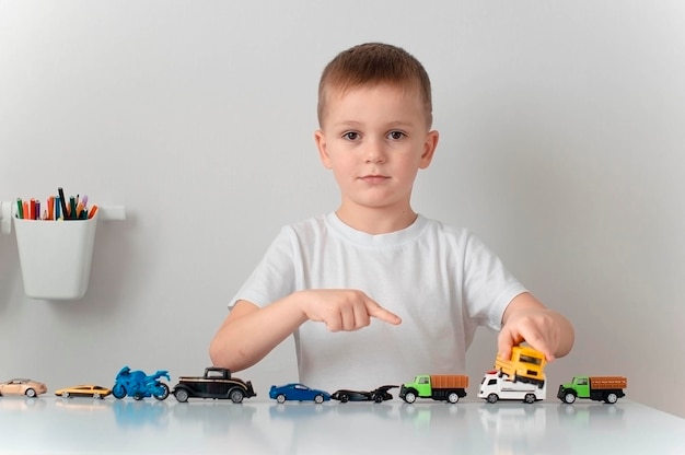 Gelukkig tevreden jongen speelt met gekleurde speelgoedautootjes aan tafel Kinderpret overdag Het kind is blij om thuis te zijn Zijn auto's zijn zijn favoriete speelgoed Het concept van de kindertijd