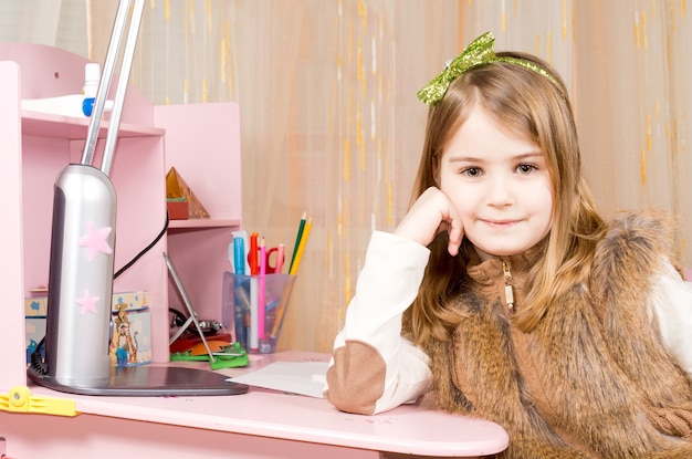 Gelukkig tevreden meisje zit aan haar roze bureau in haar slaapkamer ontspannen leunend met haar hoofd op haar hand kijken naar de camera met een glimlach